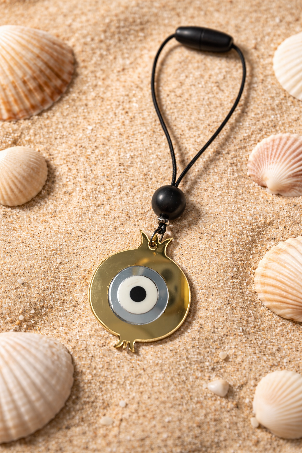 Evil eye pendant on a black cord with seashells on sand