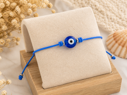 Handmade adjustable blue cord bracelet with a traditional Greek evil eye bead, worn on the wrist.