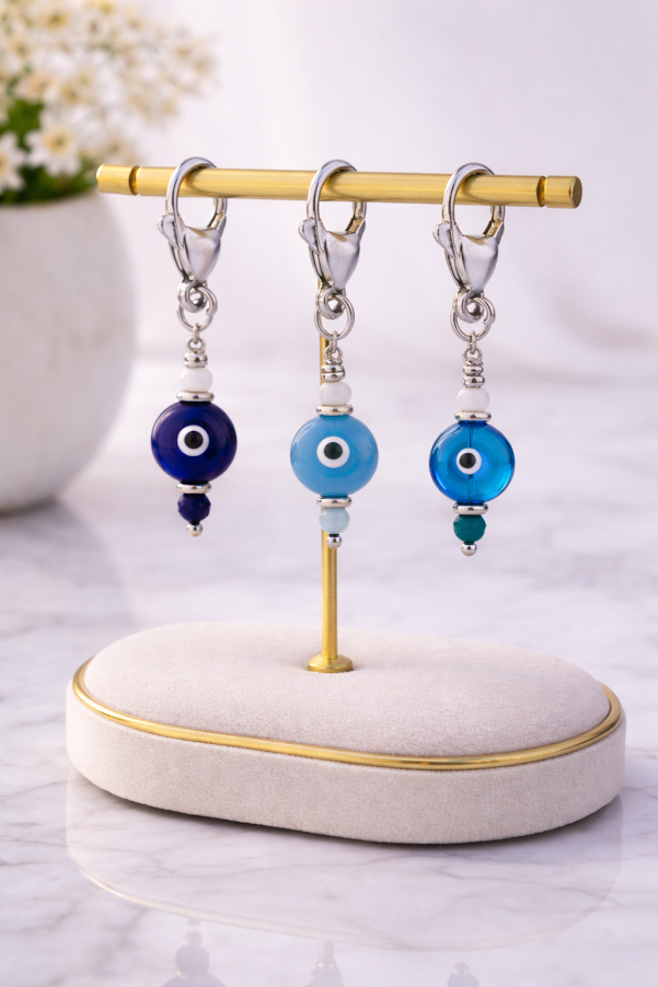 Three pairs of earrings with blue evil eye beads on a gold stand.