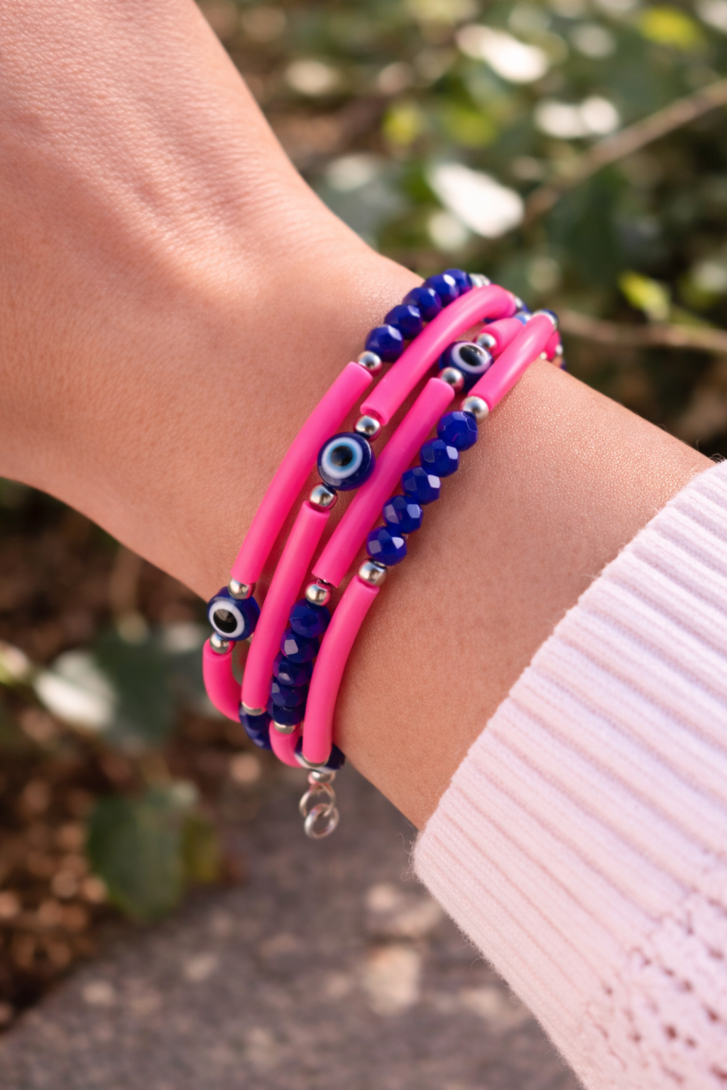 Close-up of a wrist wearing pink and blue beaded bracelets with a blurred natural background