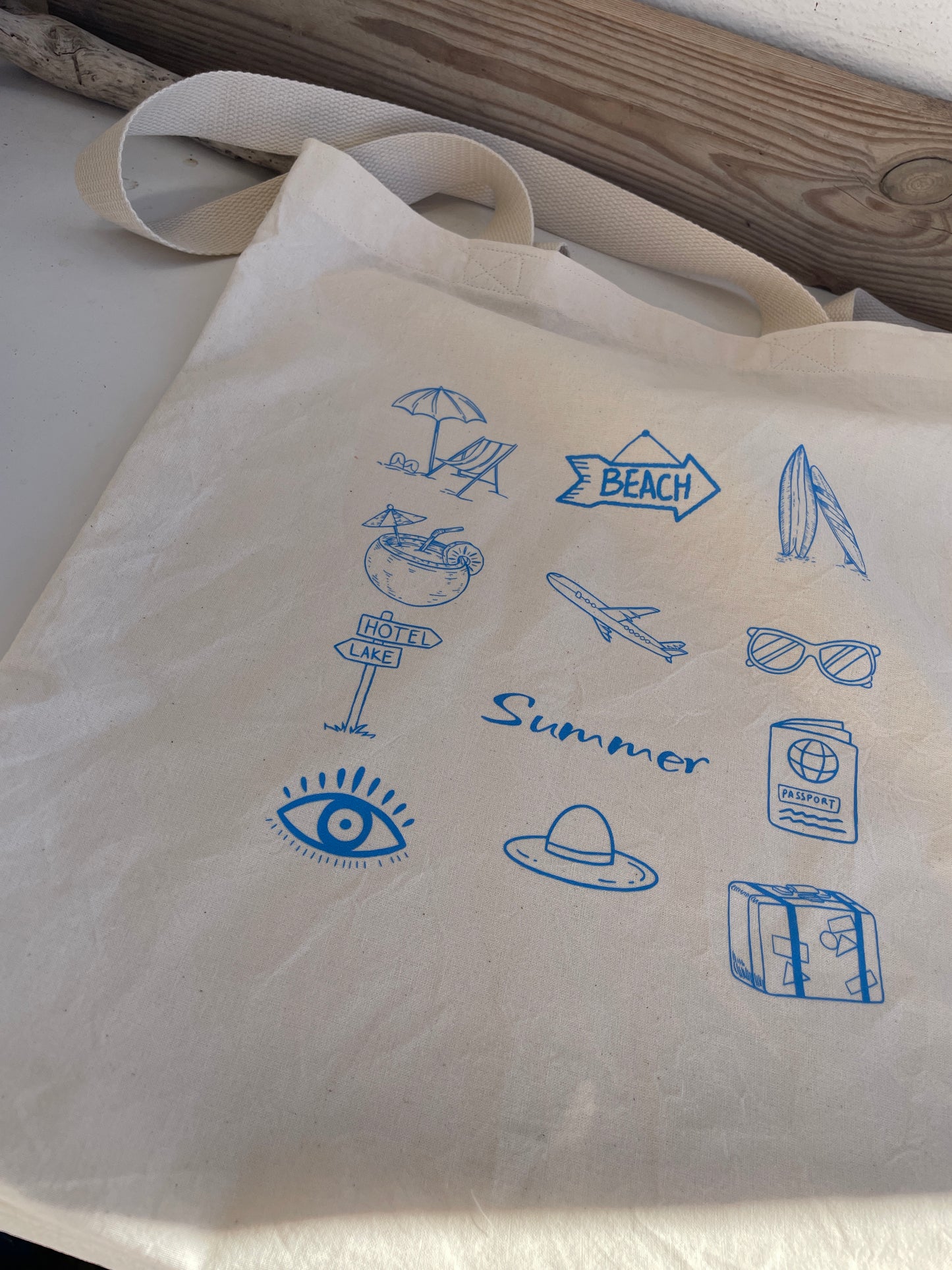 Beige tote bag with blue summer-themed icons on a wooden surface