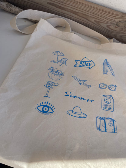 Beige tote bag with blue summer-themed icons on a wooden surface