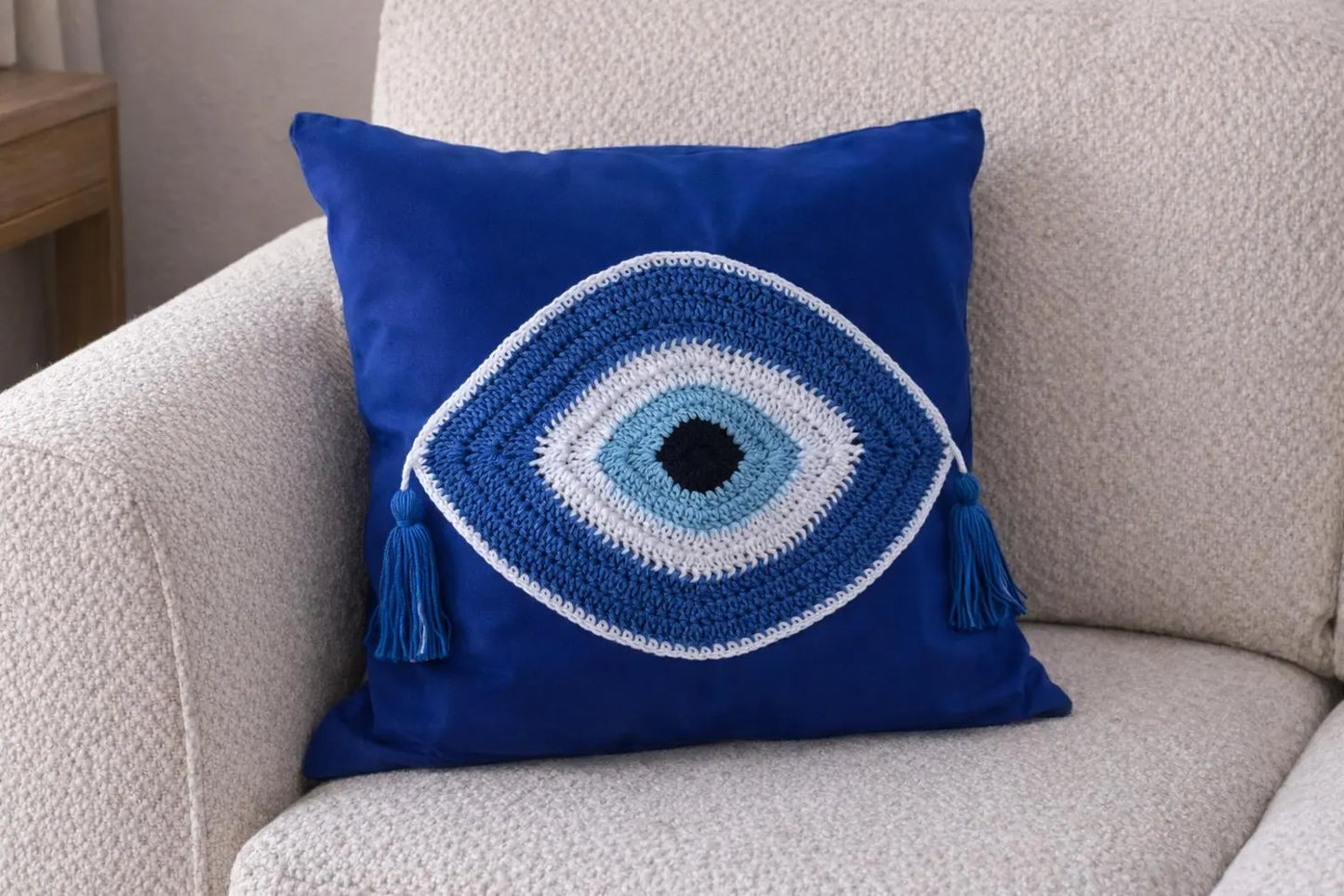 Blue pillow with eye design and tassels on a beige armchair