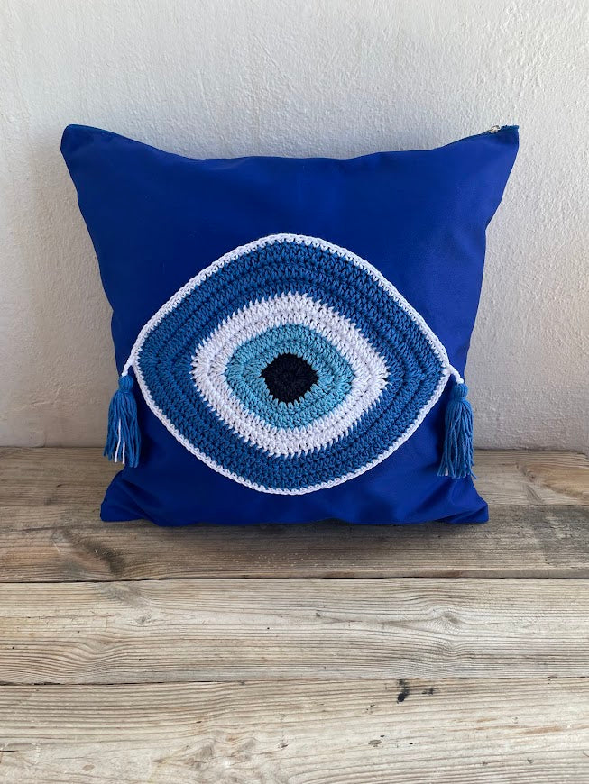 Blue pillow with a crochet eye design on a wooden surface