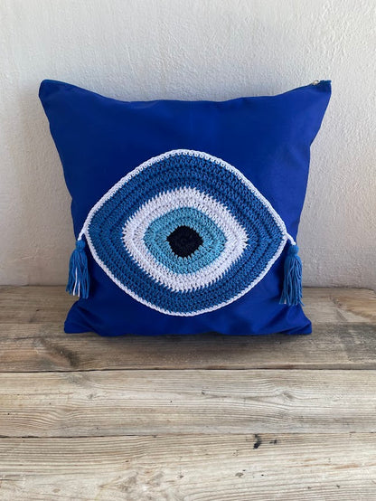 Blue pillow with a crochet eye design on a wooden surface