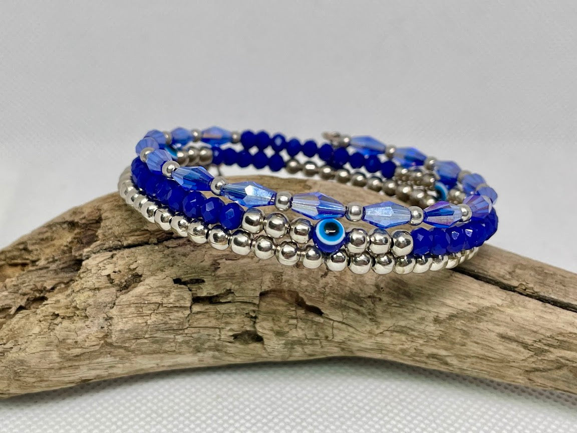 Blue beaded bracelet with silver accents on a piece of driftwood against a white background