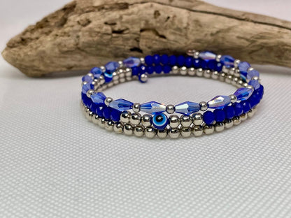 Blue beaded bracelet on a white surface with a piece of driftwood in the background