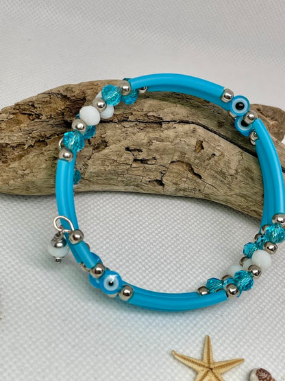 Blue beaded bracelet with silver beads on a white background with driftwood and starfish.