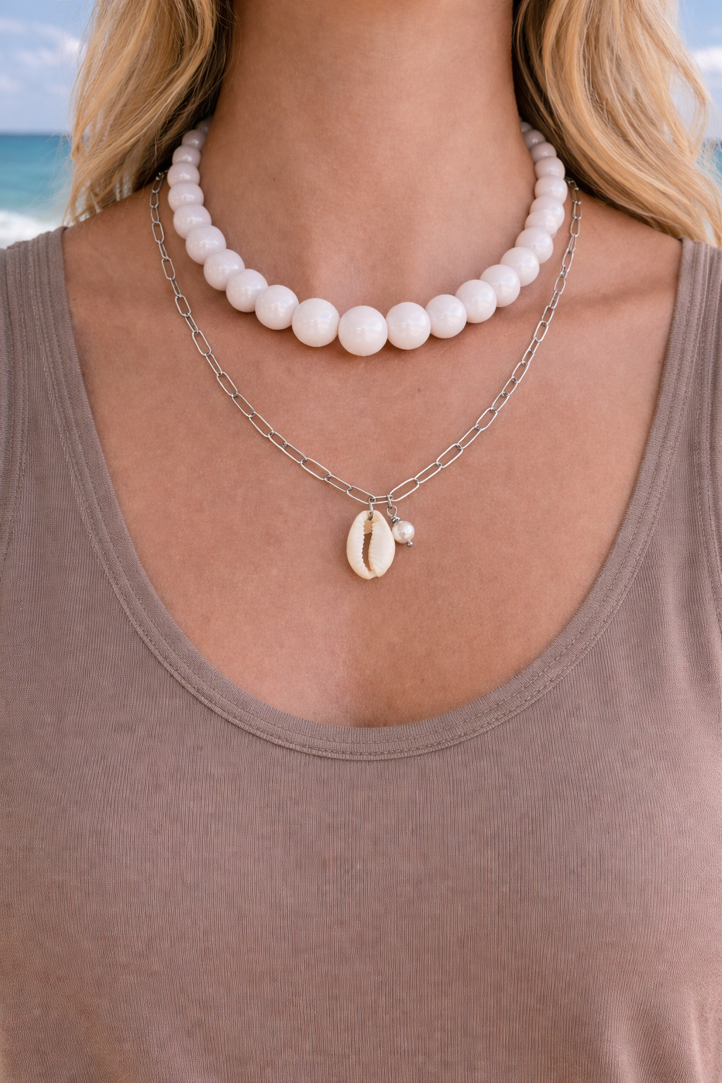 Woman wearing a pearl necklace with a shell pendant against a beach background