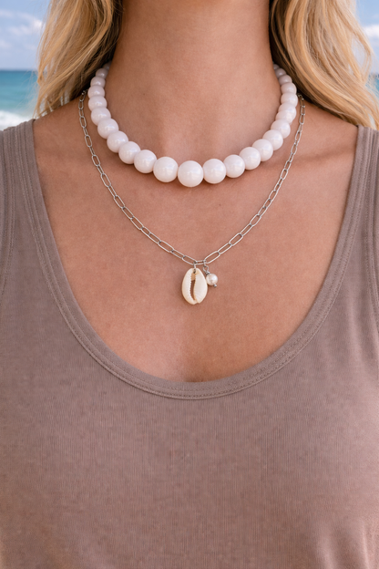 Woman wearing a pearl necklace with a shell pendant against a beach background