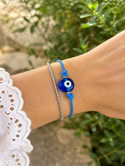 Close-up of an adjustable braided blue bracelet featuring a handmade Greek evil eye glass bead worn on the wrist.