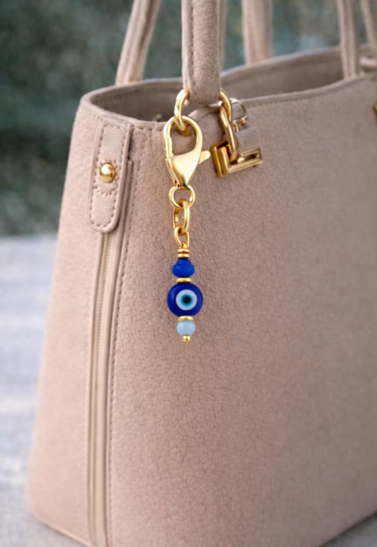 Beige handbag with a gold clasp and blue evil eye charm.