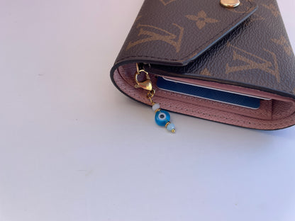 Louis Vuitton wallet with a blue evil eye charm on a white background