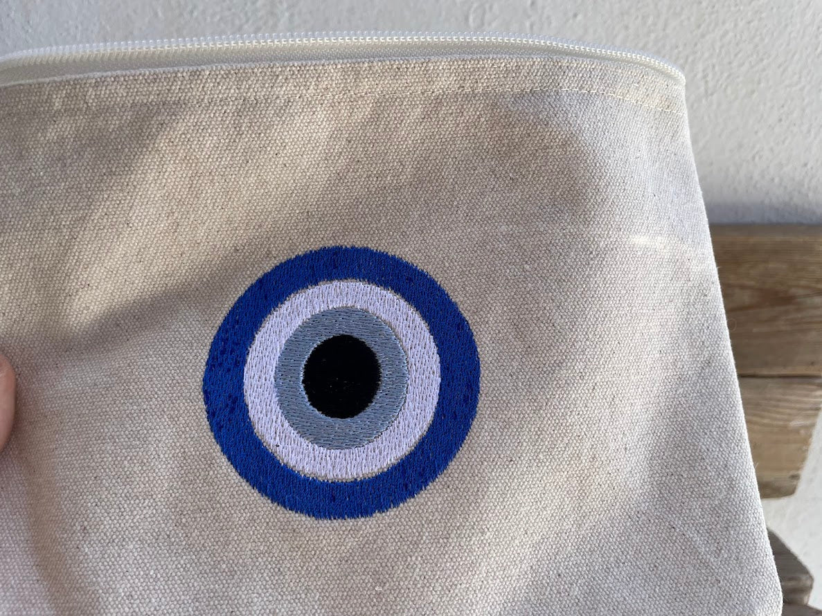 Beige pouch with a blue and white eye design on a wooden surface.