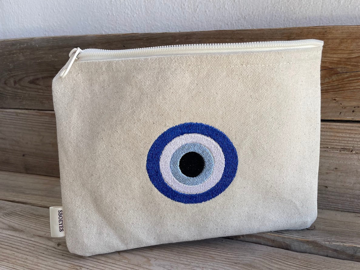 Beige pouch with a blue and black eye design on a wooden surface