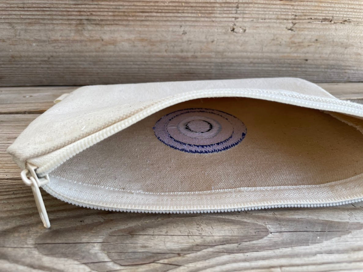 Beige pouch with a purple circular design on a wooden surface