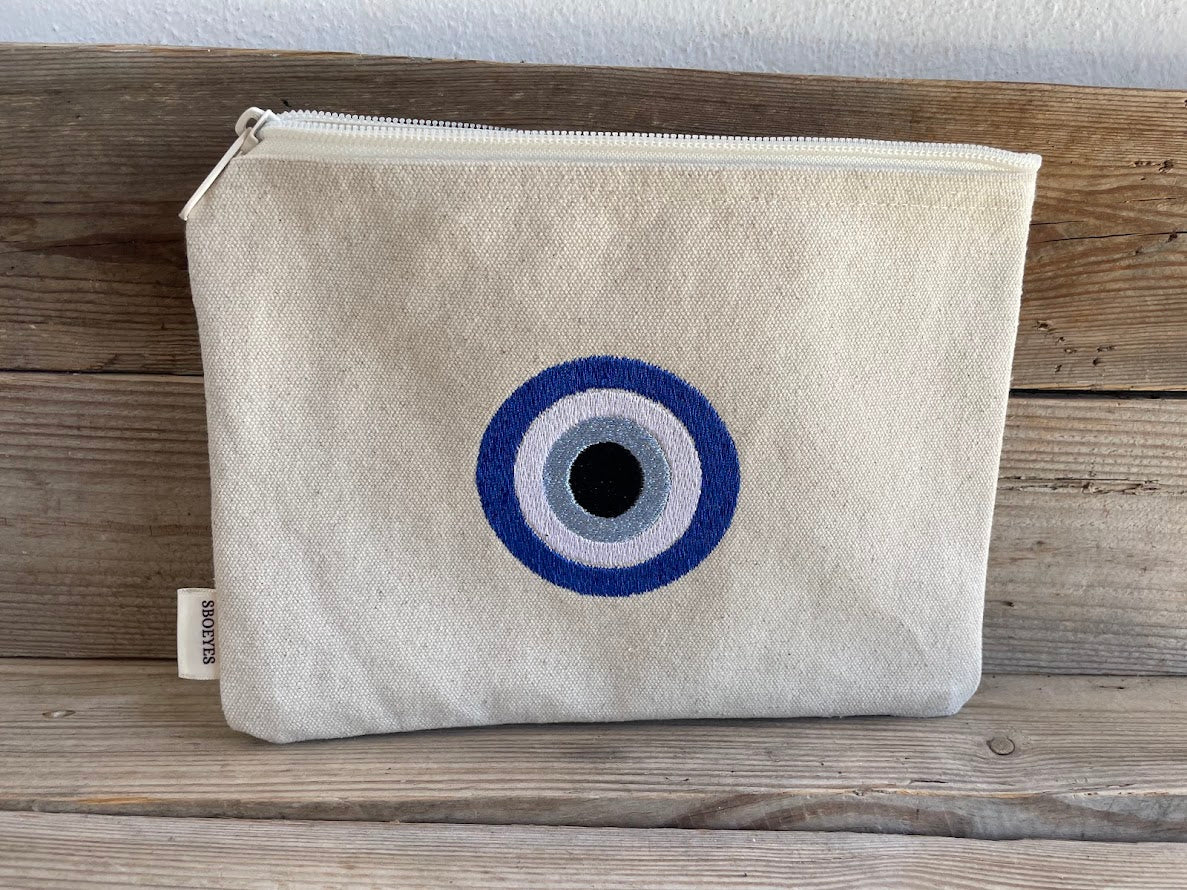Beige pouch with a blue and gray eye design on a wooden surface