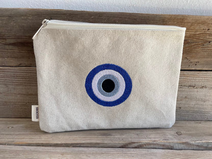 Beige pouch with a blue and gray eye design on a wooden surface