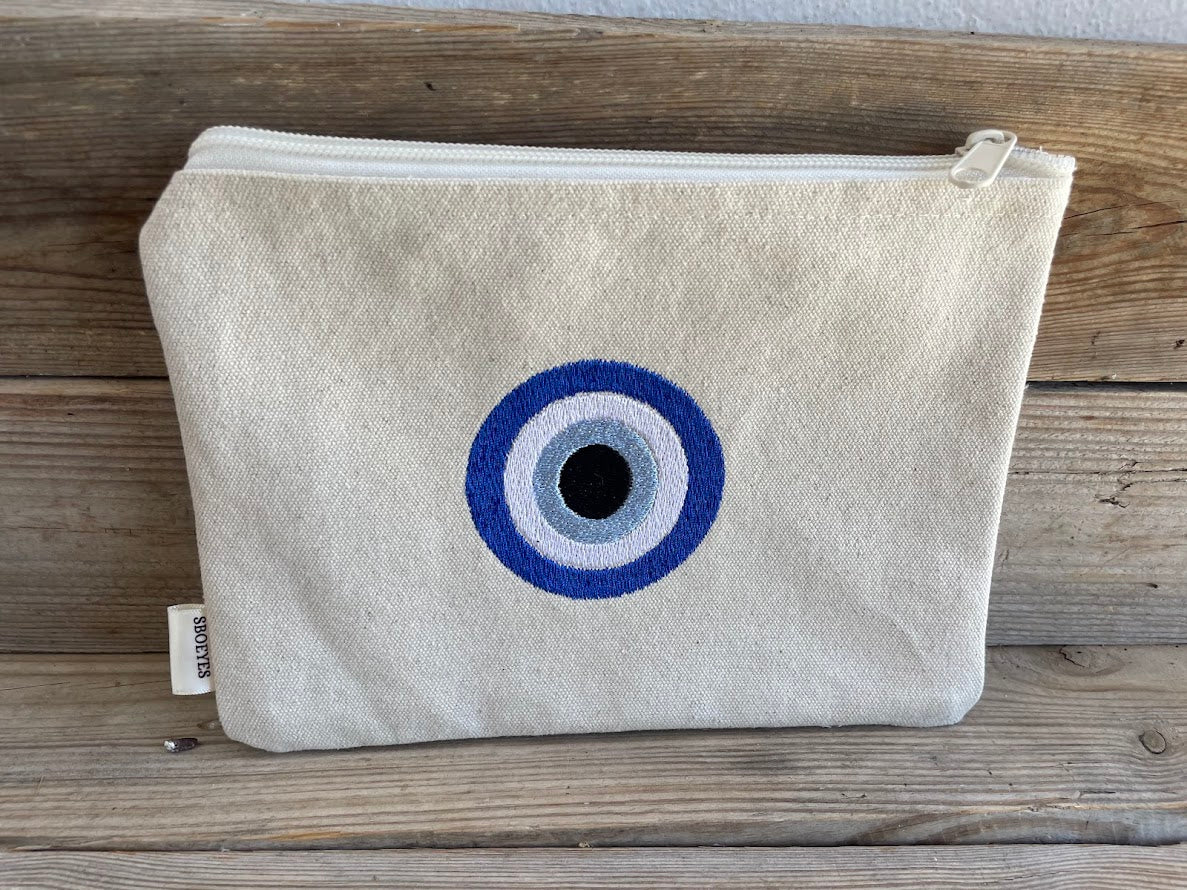 Beige pouch with a blue and black eye design on a wooden surface