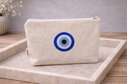 Beige pouch with blue and black eye design on a marble surface