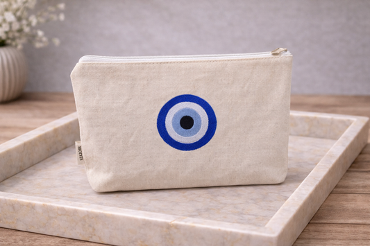 Beige pouch with blue and black eye design on a marble surface