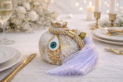 Decorative table setting with a decorative ceramic pomegranate and tassel on a white tablecloth.