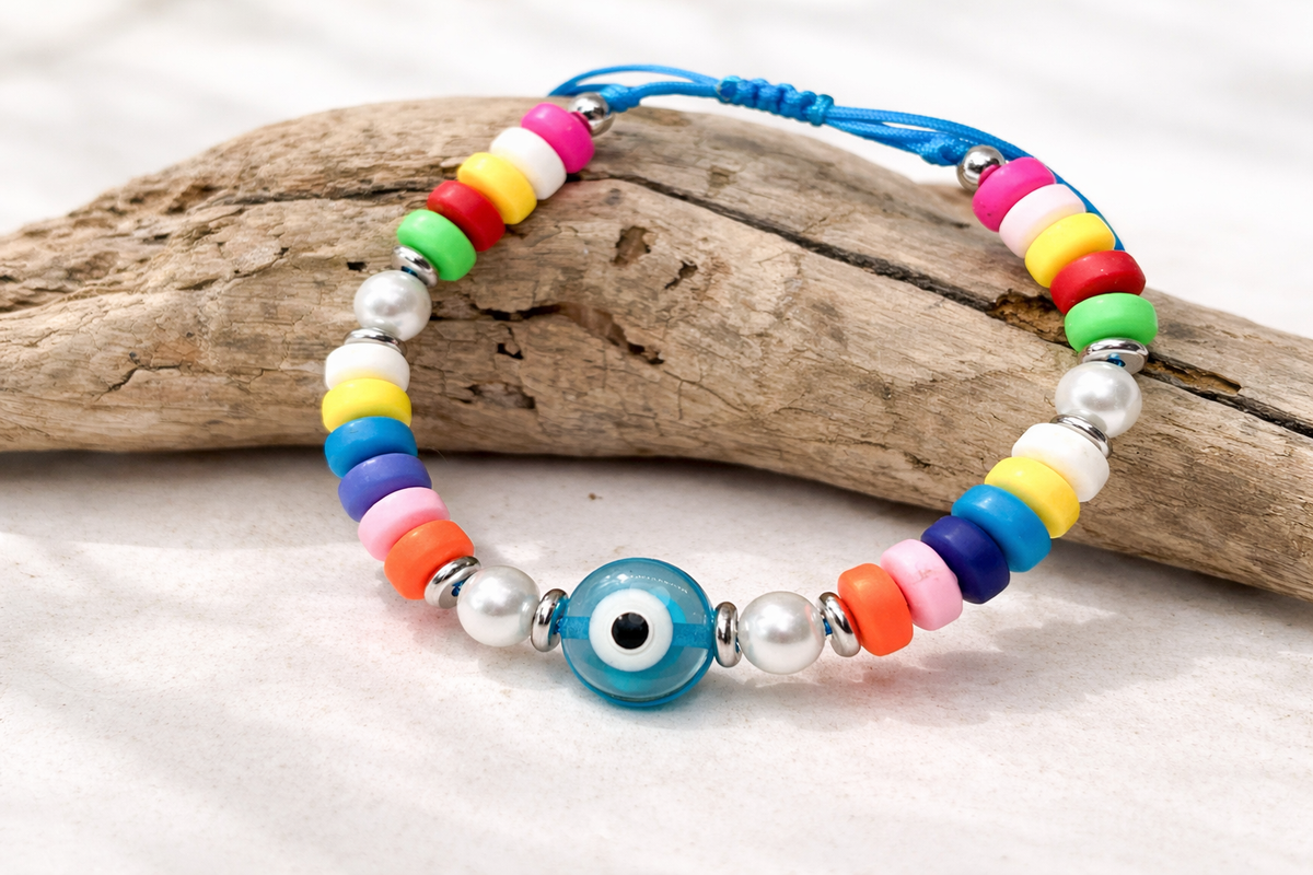 Colorful beaded bracelet with a blue evil eye charm on a piece of driftwood.