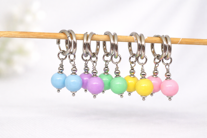 Set of colorful beaded stitch markers on a wooden stick against a white background