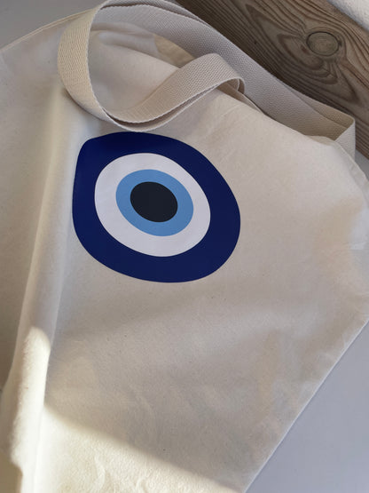 Beige tote bag with a blue and white circular design on a wooden surface.