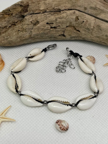 Bracelet with cowrie shells and starfish on a white surface with driftwood in the background