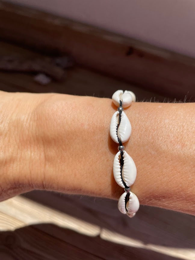 Bracelet with cowrie shells on a wrist against a neutral background