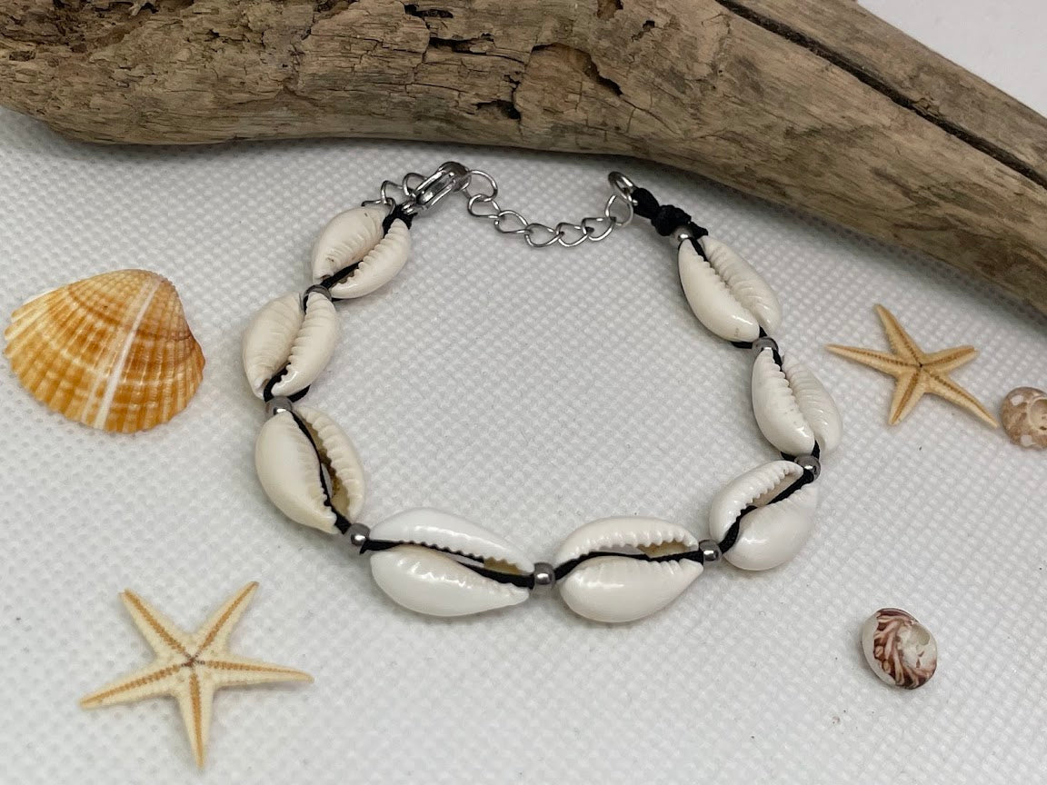 Bracelet made of cowrie shells on a textured surface with starfish and shells.