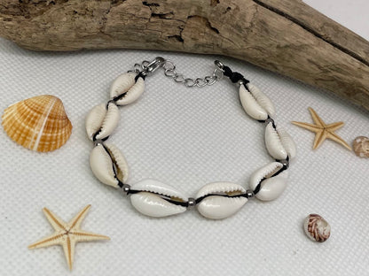 Bracelet made of cowrie shells on a textured surface with starfish and shells.