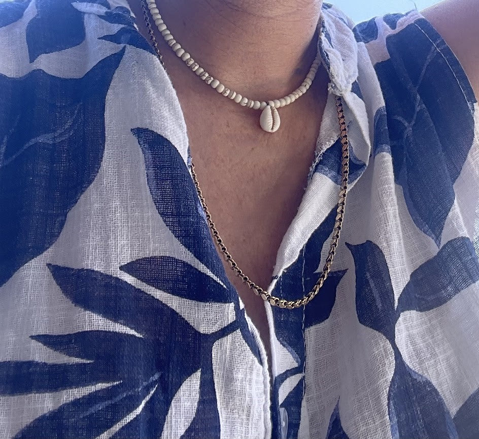 Person wearing a blue and white patterned garment with a necklace and shell pendant.