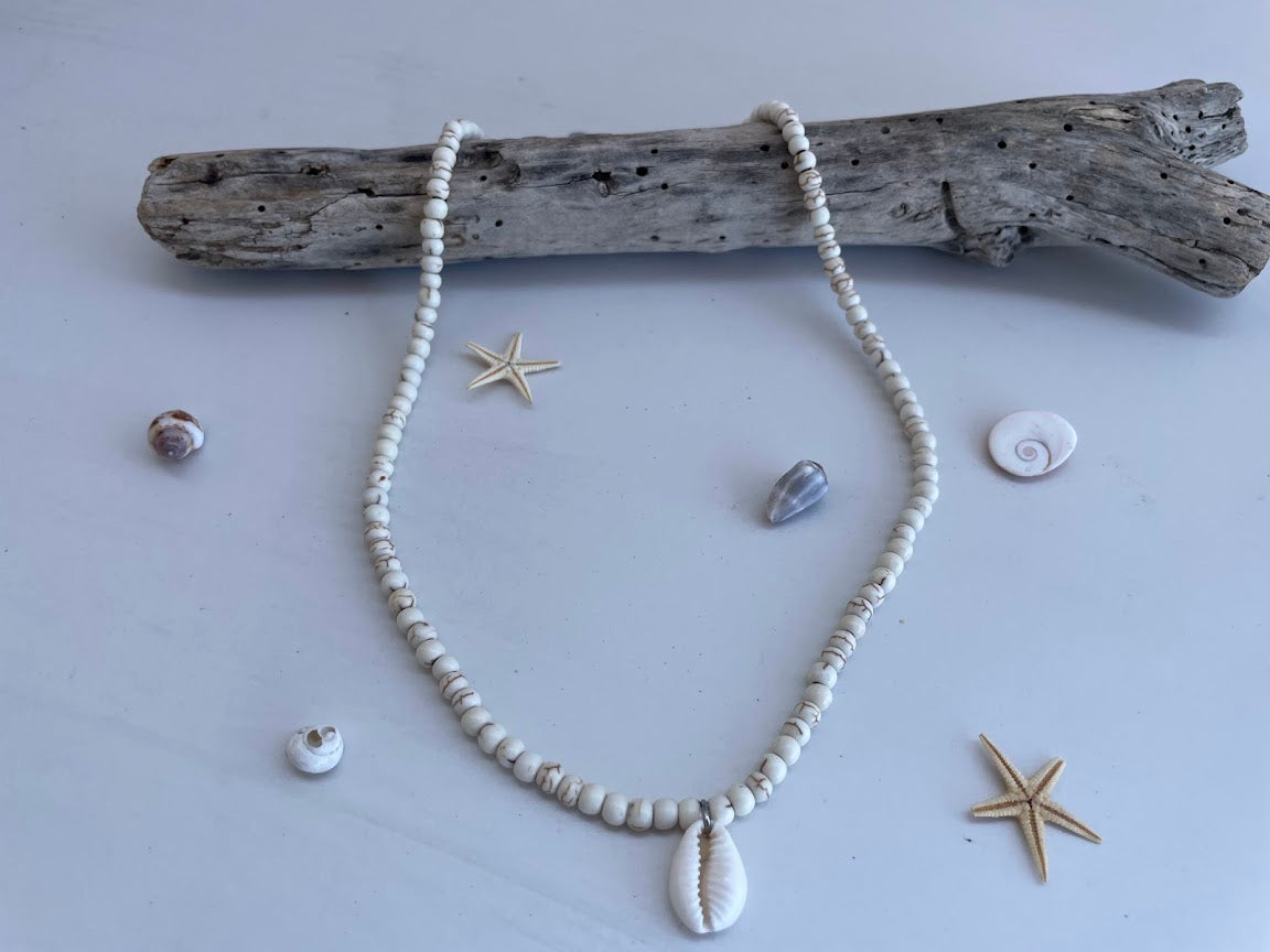 Necklace with shell pendant on a light gray background with driftwood and shells.