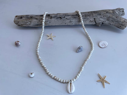Necklace with shell pendant on a light gray background with driftwood and shells.