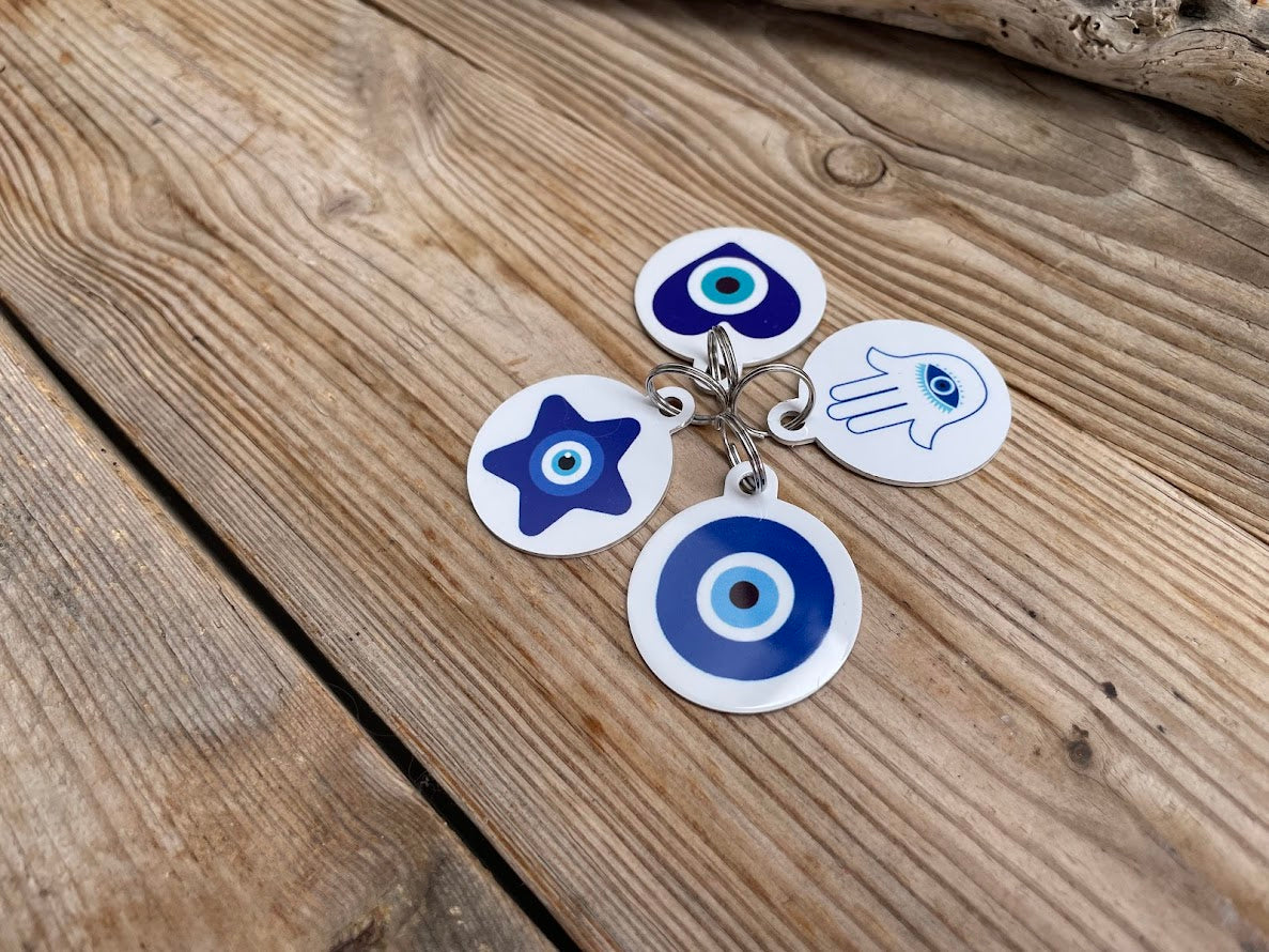 Three custom dog tags with evil eye design in blue and white, attached to a blue and white striped collar, displayed on a wooden surface.