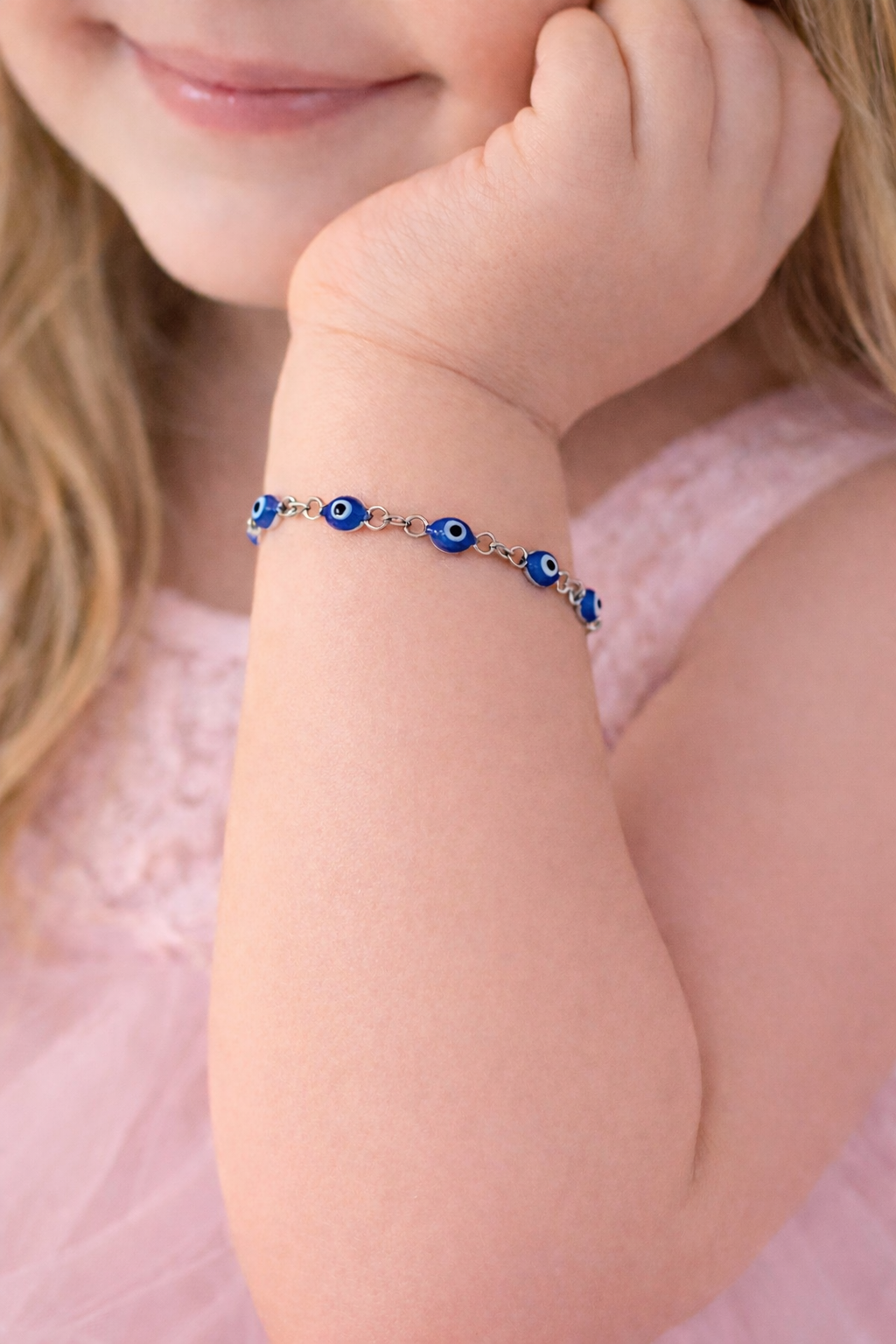 Child wearing a bracelet with blue beads on a pink background