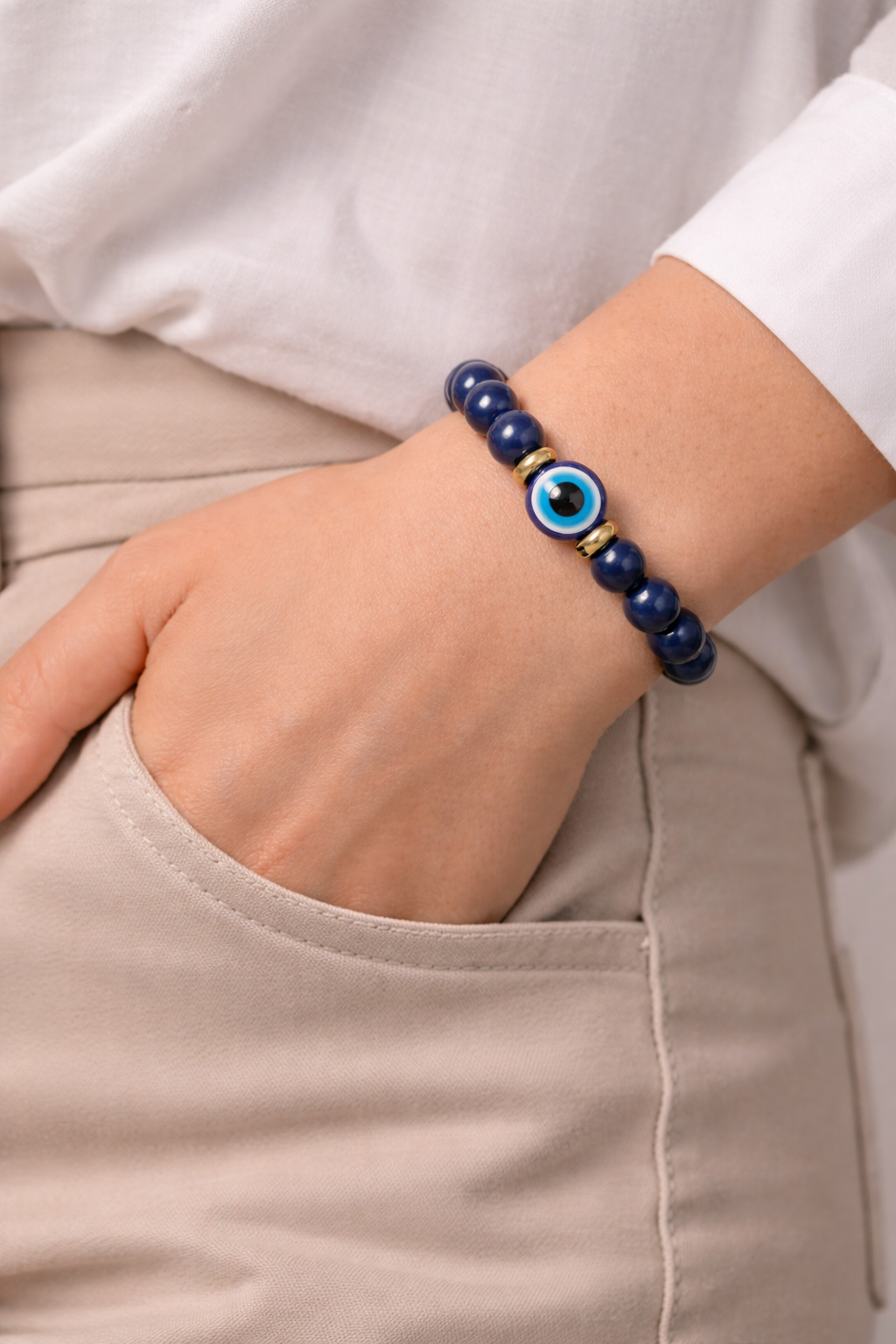 Hand wearing a blue beaded bracelet with an evil eye charm on a plain background