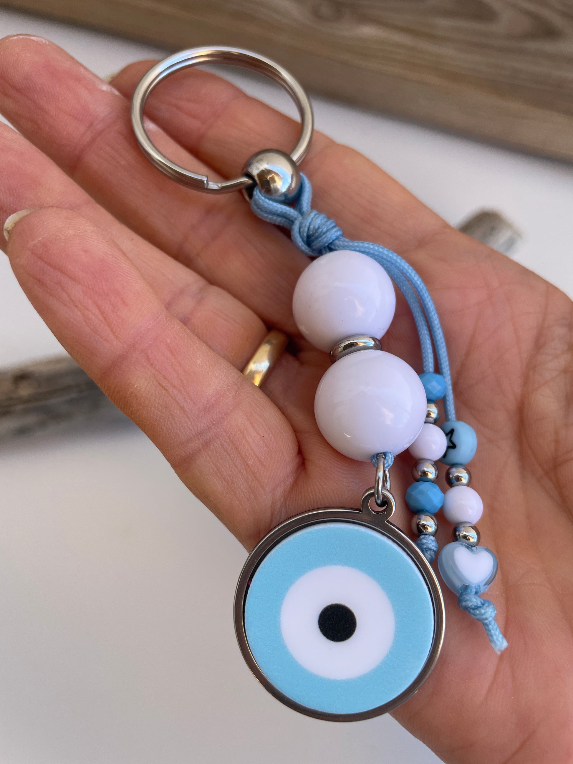 Hand holding a keychain with beads and an eye design against a neutral background