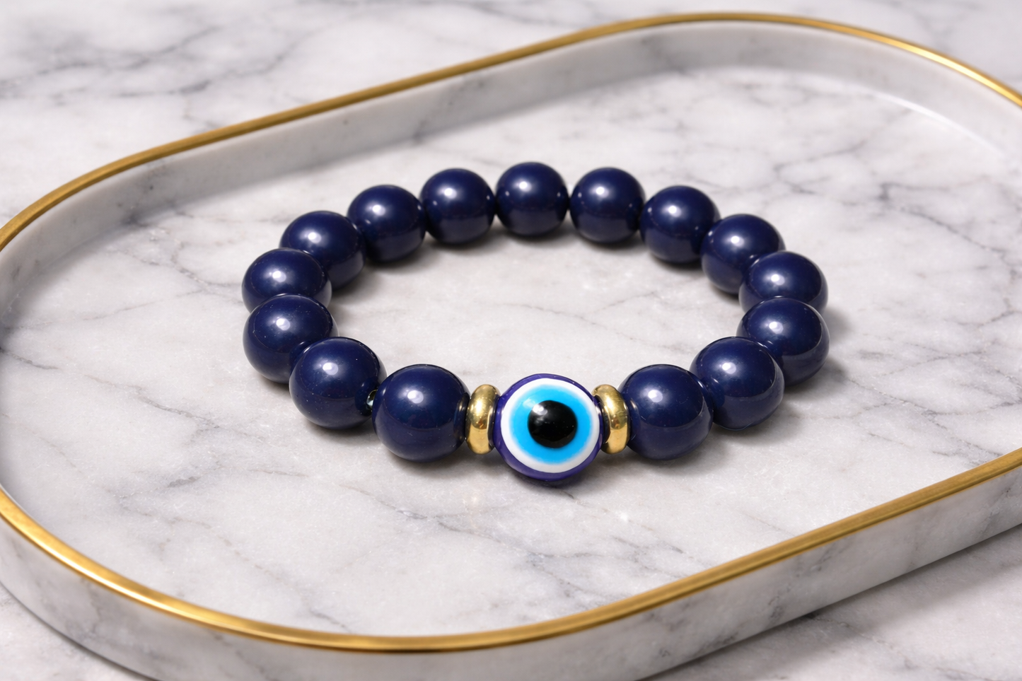 Navy blue beaded bracelet with a central evil eye charm on a marble surface