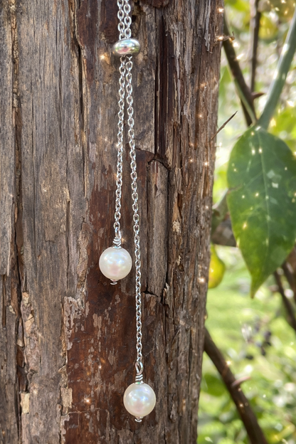 Silver necklace with pearl pendants hanging on a wooden surface with greenery in the background