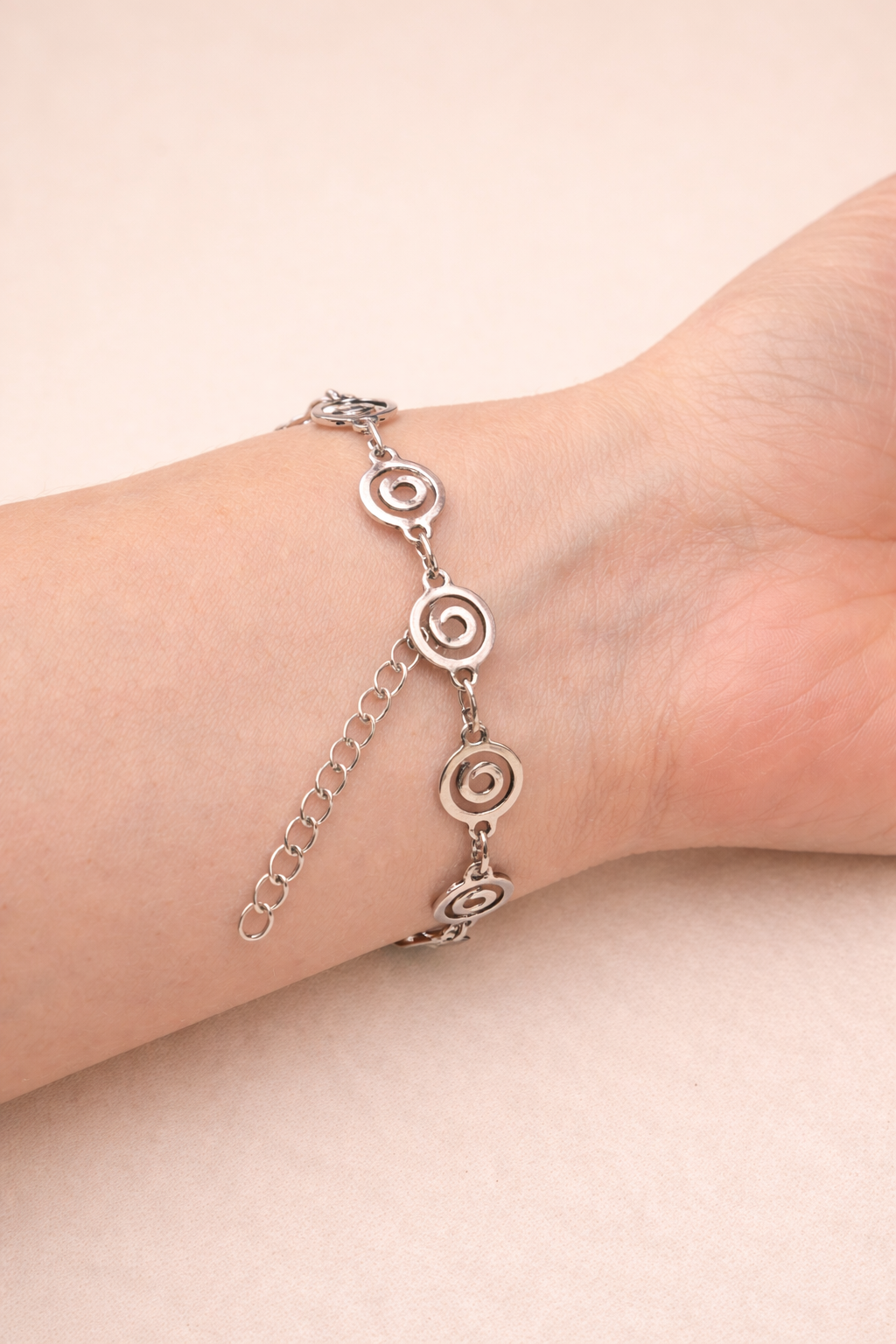 Silver anklet with circular designs on a person's ankle against a beige background