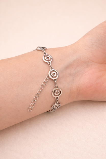 Silver anklet with circular designs on a person's ankle against a beige background