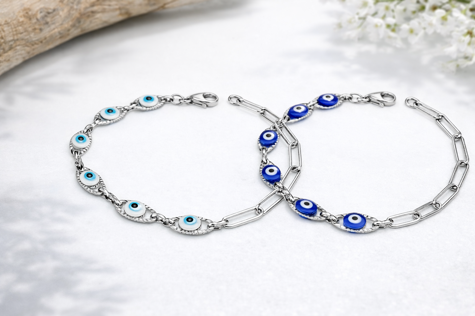 Two silver bracelets with blue evil eye charms on a light background