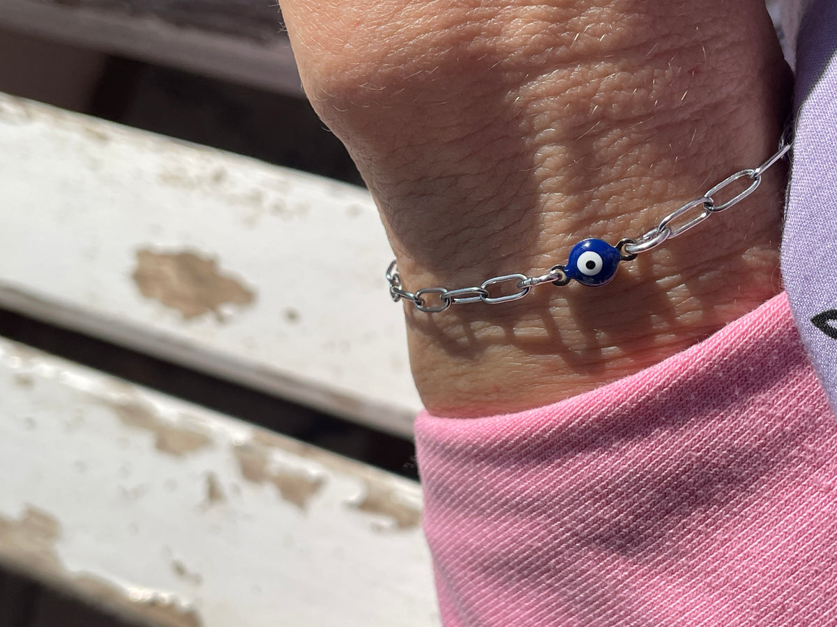 Bracelet with a blue evil eye charm on a wrist, with a blurred background.