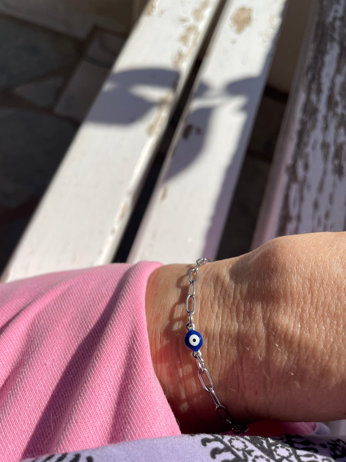 Person wearing a silver bracelet with an eye charm on a pink sleeve.