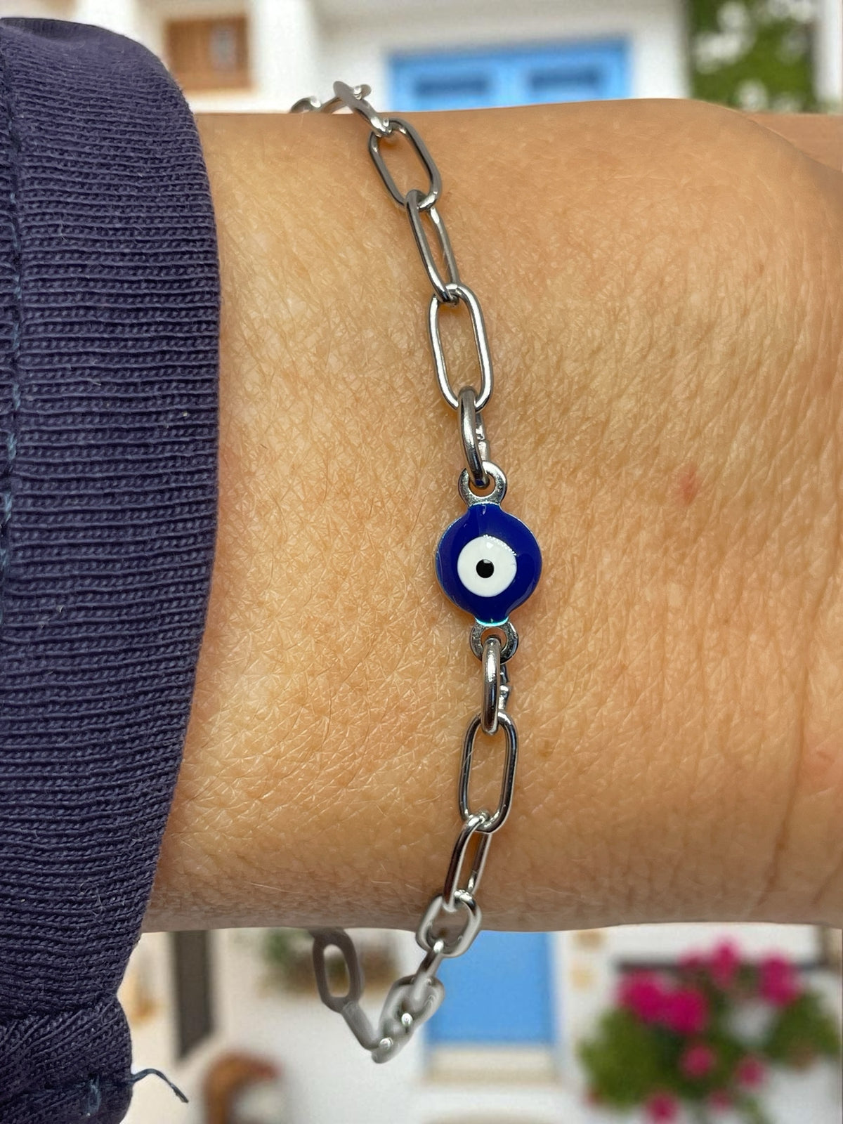 Silver chain bracelet with an eye charm on a wrist, blurred indoor background