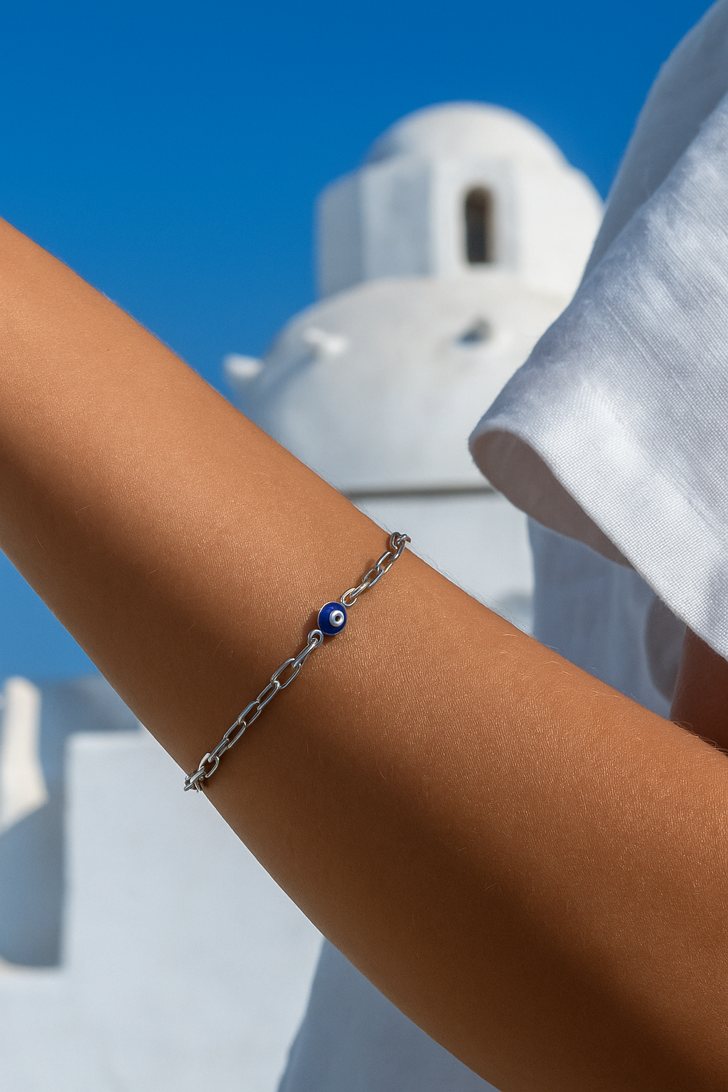Bracelet with a blue bead on a person's wrist against a blue sky and white building background