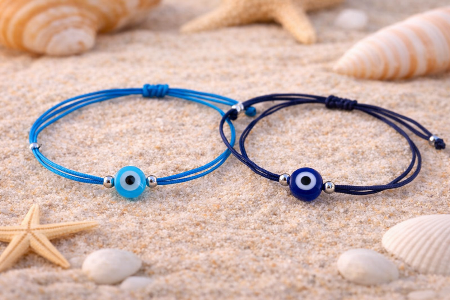Two blue bracelets with evil eye beads on a sandy background with shells and starfish.